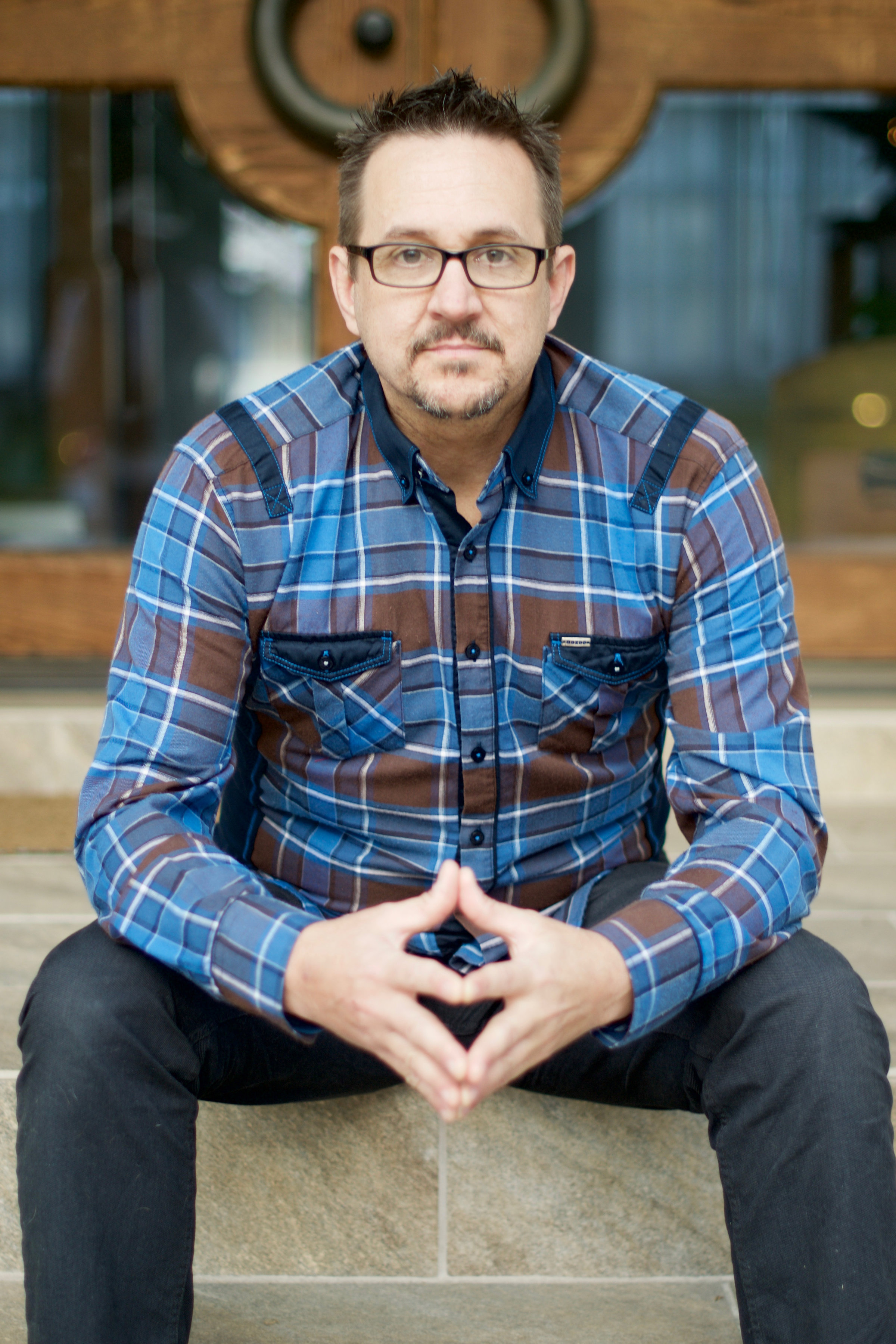 Paul Loggins wearing blue plaid shirt sitting on stairs